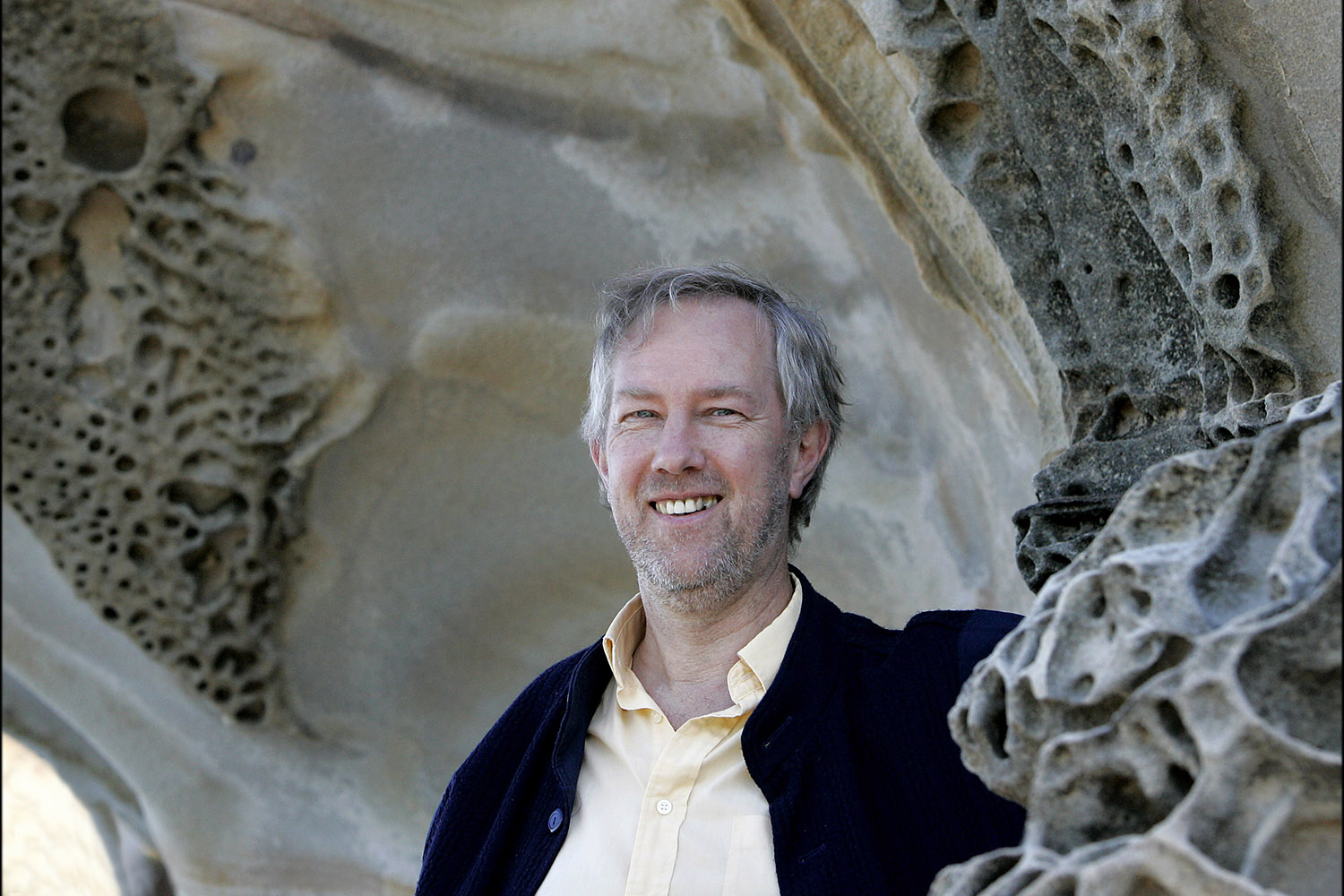 A man with grey hair smiling in front of a stone structure