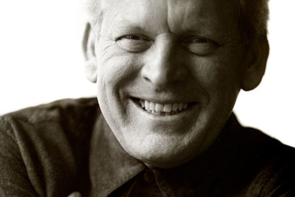 A black and white photo of Sir Thomas Allen smiling at the camera