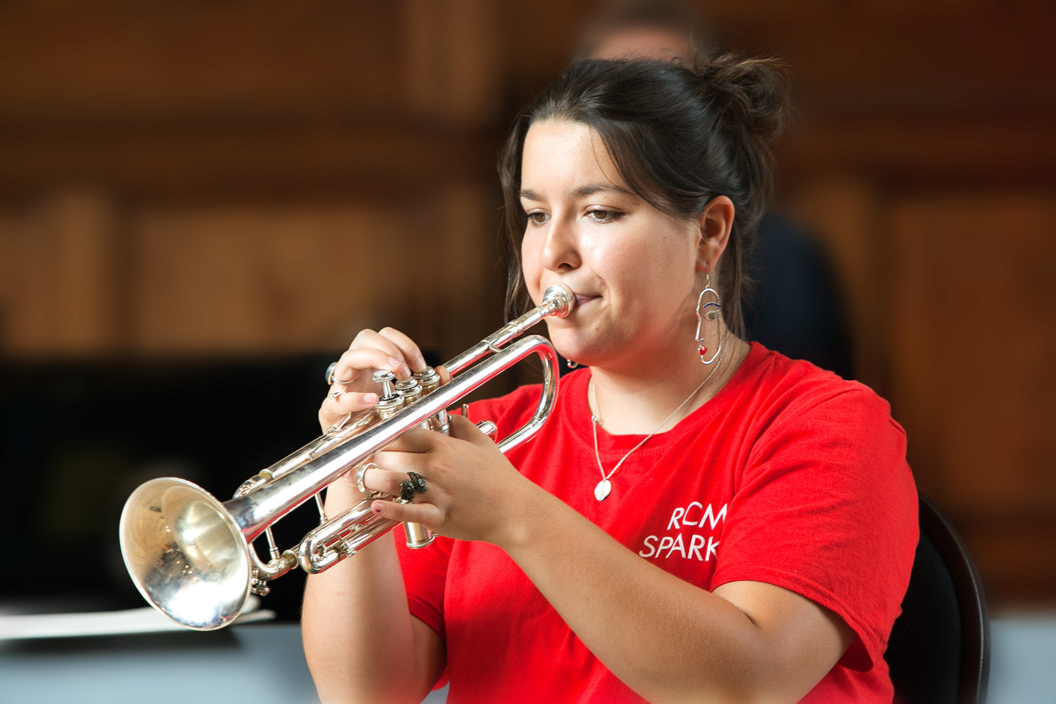 A lady wearing a red t-shirt plays a trumpet