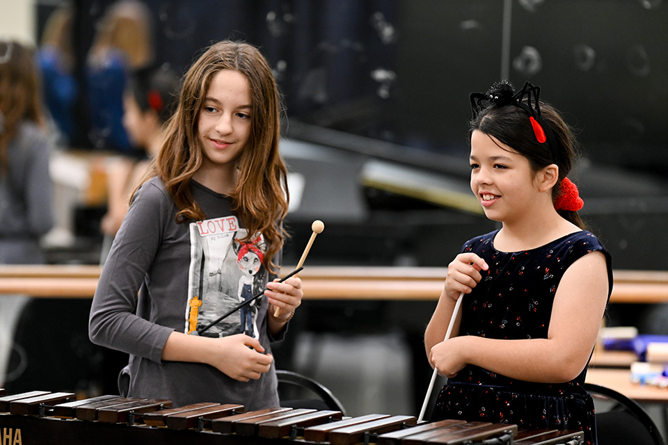 Two girls play a marimba, smiling