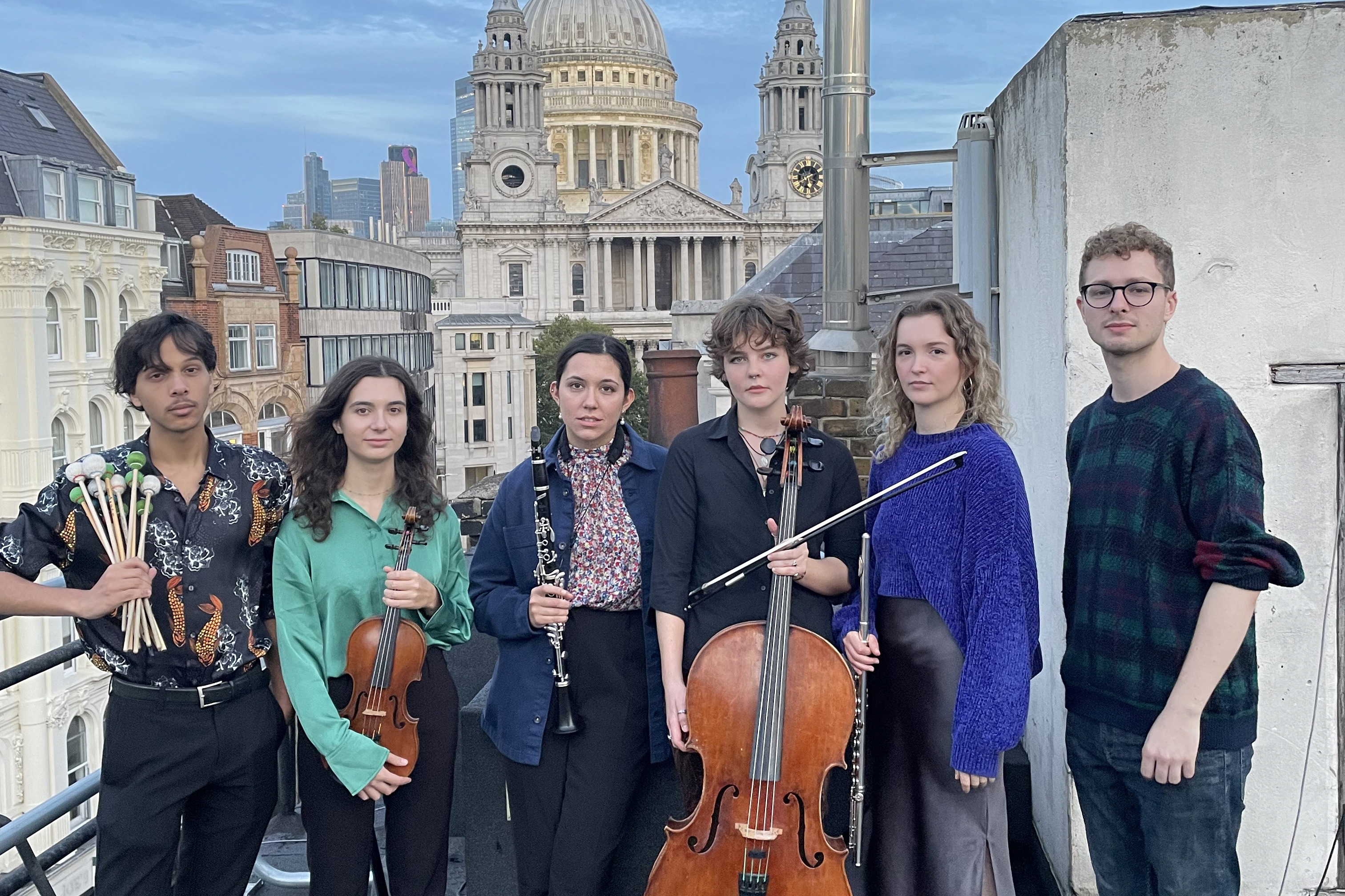 A group of musicians holding percussion and string instruments standing on a London rooftop