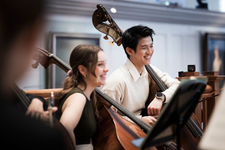 Two double bassists smile as they hold their instruments on stage