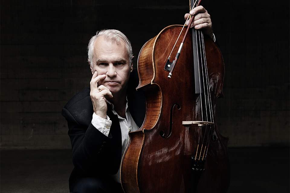 Torleif Thedéen crouches next to his cello holding it with one hand, resting his chin in the other