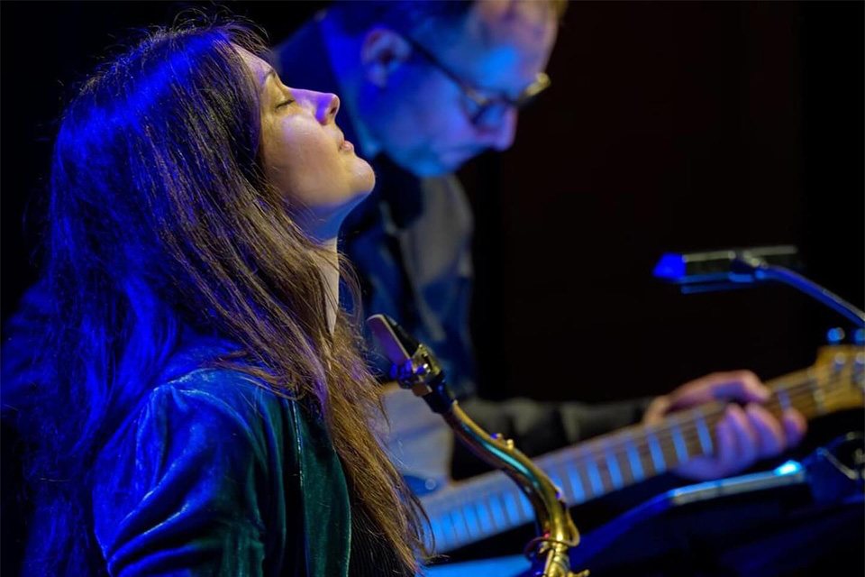 Trish Clowes holds her saxophone mid-performance on stage and looks up