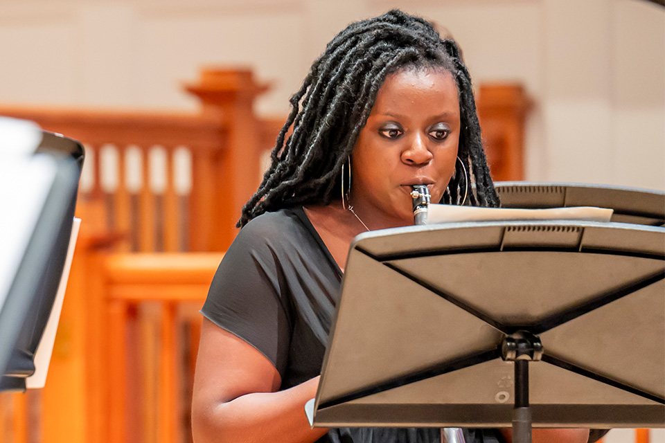 A young woman wearing a black dress plays the clarinet on stage