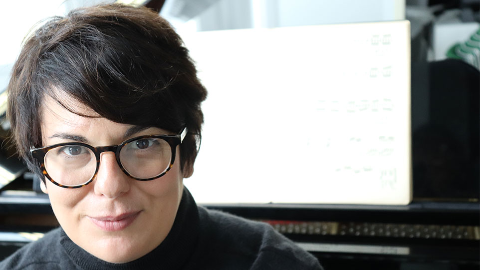 Inja Stanović: A woman with glasses is seated at a piano, engaged in playing, with sheet music visible in front of her.