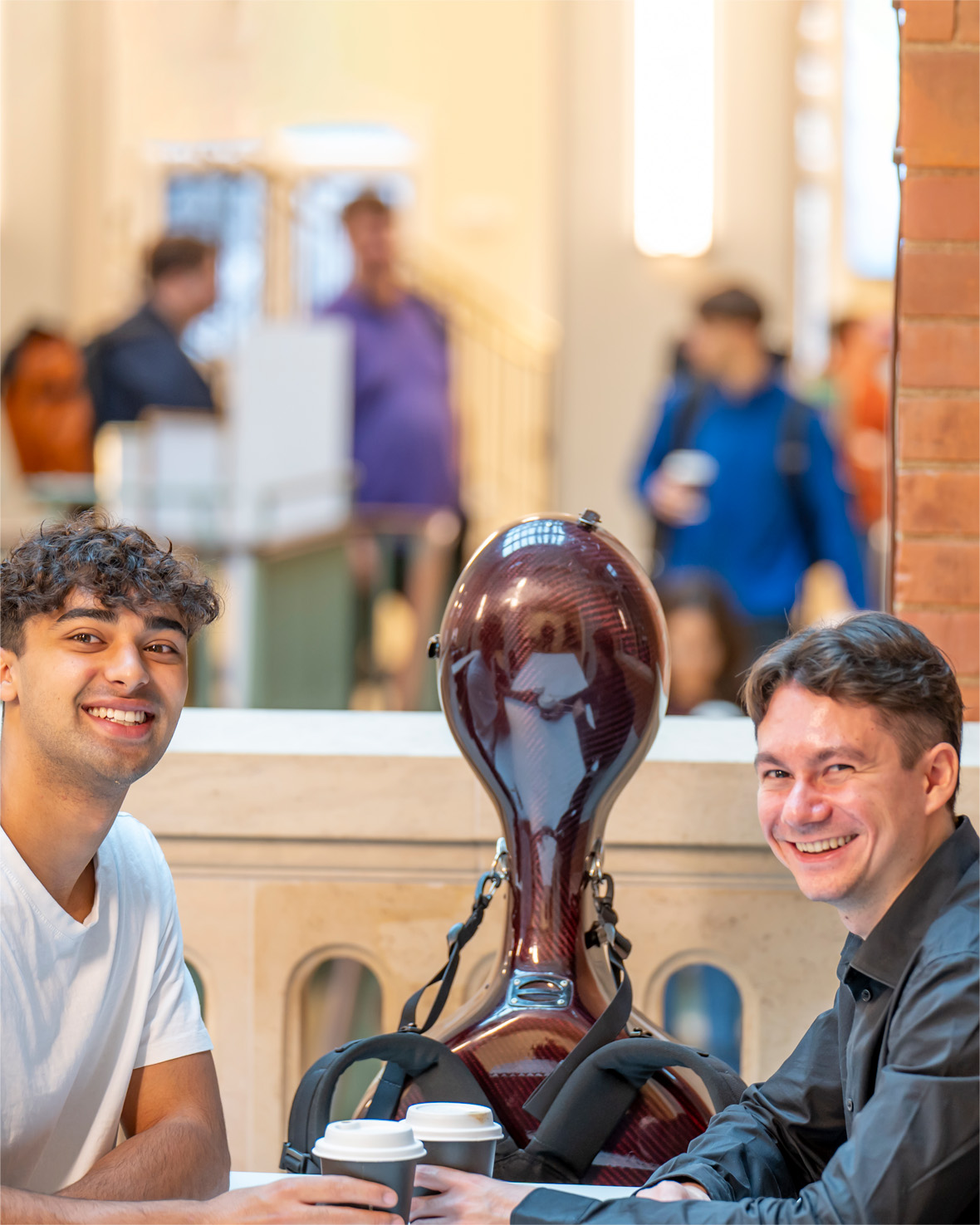 Two men, wearing casual clothes, holding two coffee cups, with double bass case.