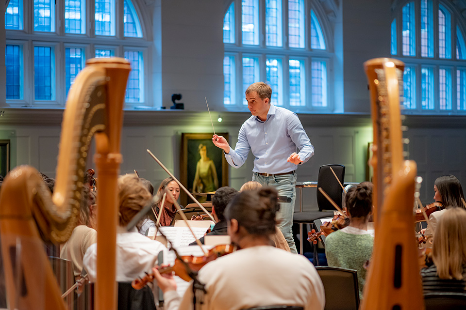 A man holding a baton in front of an orchestra test